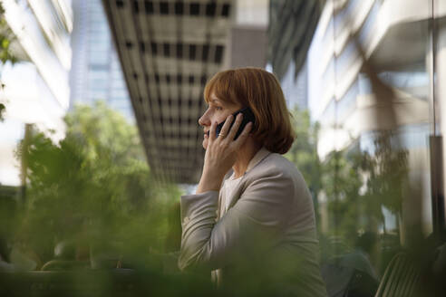 Reife Geschäftsfrau mit braunen Haaren im Gespräch mit einem Smartphone - IKF00090