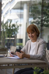 Smiling businesswoman doing video call sitting at sidewalk cafe - IKF00106