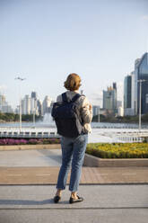 Geschäftsfrau mit Rucksack, die auf einem Fußweg stehend Gebäude betrachtet - IKF00119