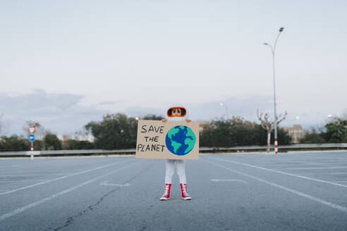 Girl dressed as astronaut showing Save The Planet cut out standing in parking lot - JCZF01241