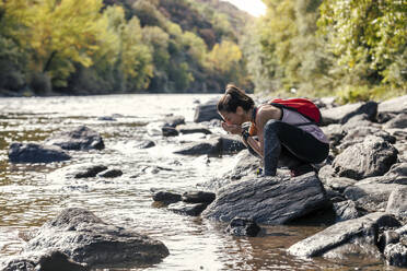 Thirsty woman drinking water from river - JSRF02482