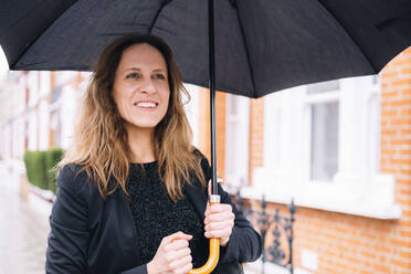 Happy woman holding black umbrella - AMWF01293