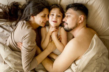 Happy parents lying with son on bed at home - ANAF01223