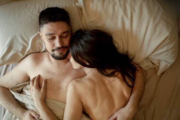 Mann umarmt schlafende Frau auf dem Bett zu Hause - ANAF01224