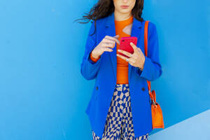 Frau, die mit ihrem Smartphone vor einer blauen Wand im Internet surft - EGHF00744