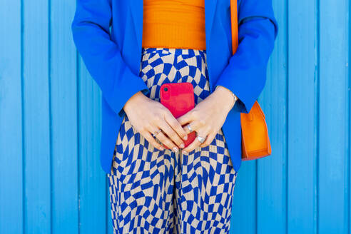 Stehende Frau mit rotem Smartphone vor blauer Wand - EGHF00746