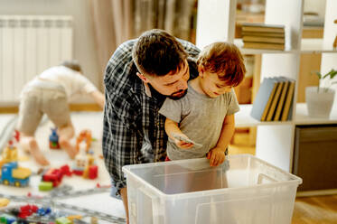 Vater und Sohn auf der Suche nach Spielzeug in einem Plastikbehälter zu Hause - ANAF01229