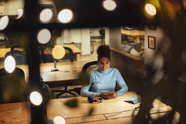 Smiling businesswoman sitting at desk with mobile phone in office - JOSEF18447