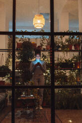 Geschäftsfrau mit Mobiltelefon bei Pflanzen in der Nacht durch Glas gesehen - JOSEF18468