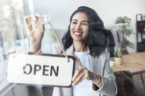 Happy businesswoman hanging open sign on door in studio - JSRF02491