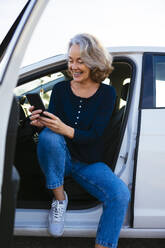 Lächelnde reife Frau, die im Auto sitzend ein Smartphone benutzt - EBSF03187