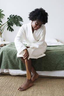 Frau massiert Bein mit Bürste im Schlafzimmer zu Hause - AAZF00252