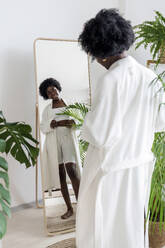 Young woman looking in mirror at home - AAZF00262