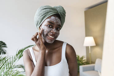 Smiling woman applying face mask at home - AAZF00288