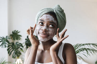 Young woman wearing towel on head and applying face mask at home - AAZF00289