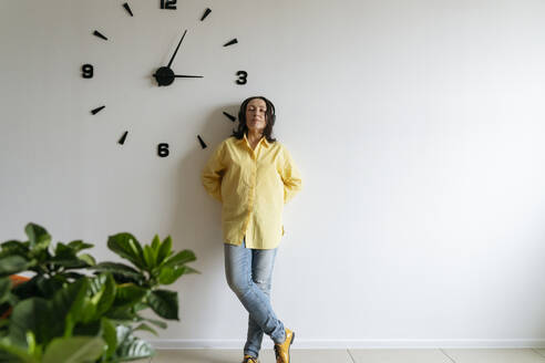 Woman wearing wireless headphones leaning on wall - OSF01519