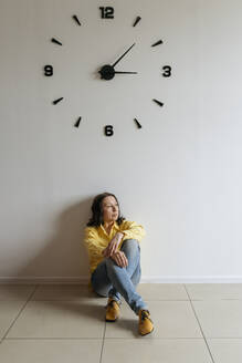 Thoughtful woman sitting under clock on floor - OSF01523