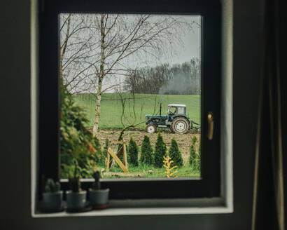 Landwirt pflügt mit Traktor auf einem Feld durch ein Fenster gesehen - VSNF00701
