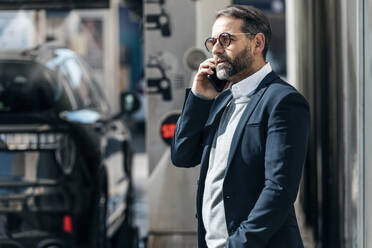 Businessman talking on smart phone standing at car wash - JSRF02504