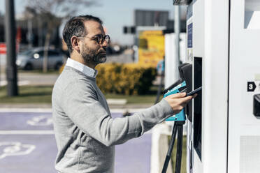 Mann bezahlt mit seinem Smartphone an einer Ladestation für Autos - JSRF02511