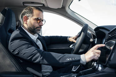 Businessman using GPS system sitting in electric car - JSRF02515