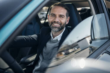 Happy businessman sitting in electric car - JSRF02517