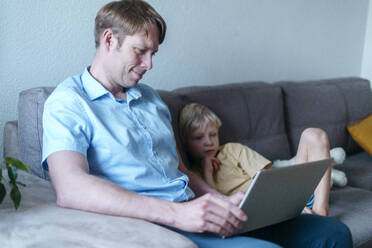 Smiling father working on laptop with son sitting in living room at home - NJAF00321