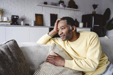 Thoughtful mature man sitting on sofa at home - EYAF02567