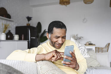 Smiling mature man using smart phone at home - EYAF02570