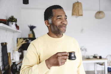 Lächelnder reifer Mann stehend mit Kaffeetasse zu Hause - EYAF02574