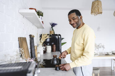 Lächelnder reifer Mann bei der Zubereitung von Kaffee in der Küche zu Hause - EYAF02583