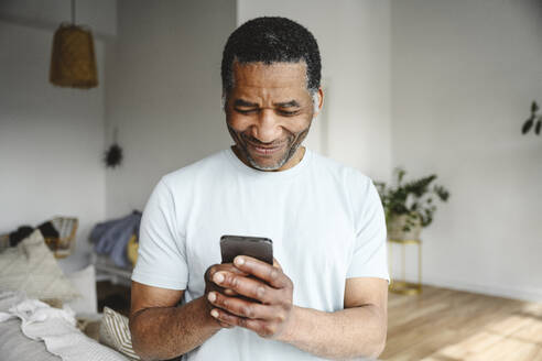 Smiling mature man using mobile phone in living room at home - EYAF02602