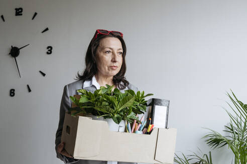 Sad businesswoman holding box with office supplies in front of wall - OSF01532