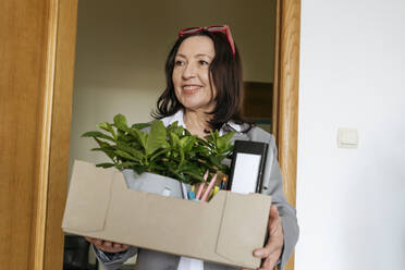 Glückliche Geschäftsfrau mit Büromaterial in einer Kiste in der Nähe der Tür - OSF01533