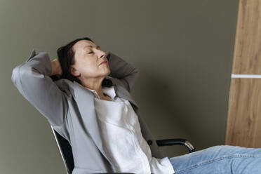 Müde Geschäftsfrau entspannt mit Händen hinter dem Kopf im Büro - OSF01539