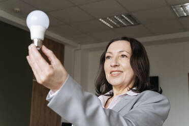Smiling businesswoman holding electric bulb at office - OSF01540