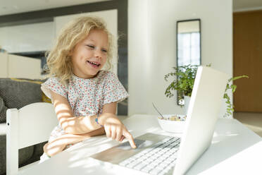 Lächelndes Mädchen mit Laptop auf dem Tisch zu Hause - SVKF01372