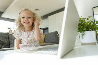 Lächelndes Mädchen mit Hand im Haar, das zu Hause am Laptop sitzt - SVKF01374