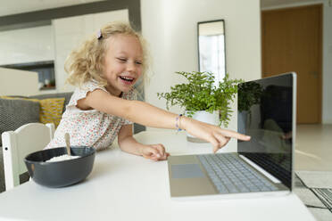 Glückliches Mädchen, das auf den Laptop-Bildschirm auf dem Tisch zu Hause zeigt - SVKF01378