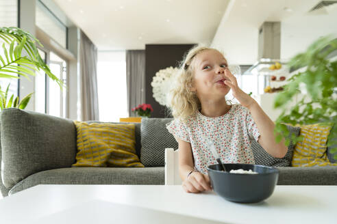 Lächelndes Mädchen genießt das Frühstück im Wohnzimmer zu Hause - SVKF01379