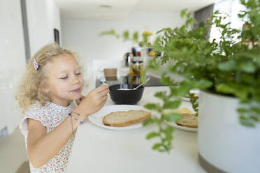 Girl putting cheese on bread at home - SVKF01382