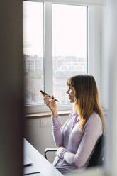 Lächelnde Geschäftsfrau, die im Büro mit einem Smartphone telefoniert - PNAF05208