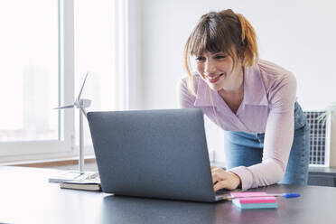 Happy businesswoman working on laptop at desk - PNAF05222