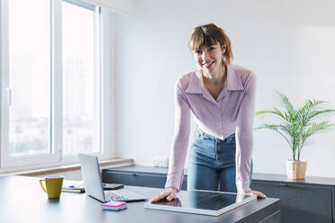 Smiling businesswoman with solar panel standing at desk - PNAF05228