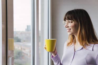 Smiling businesswoman with coffee cup looking through window - PNAF05231