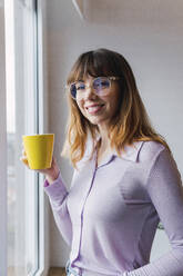 Happy businesswoman with coffee cup standing by window - PNAF05232