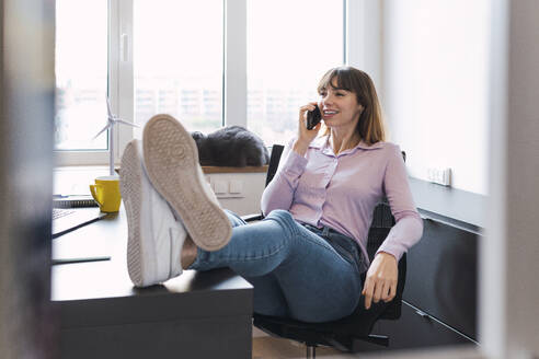 Lächelnde Geschäftsfrau, die im Büro mit einem Mobiltelefon spricht - PNAF05237