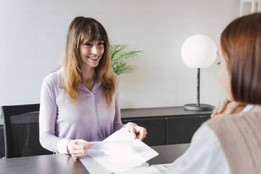 Zufriedener Immobilienmakler, der mit einem Kunden im Büro über Dokumente diskutiert - PNAF05241