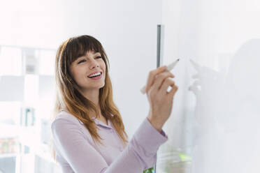 Happy businesswoman writing on whiteboard - PNAF05252