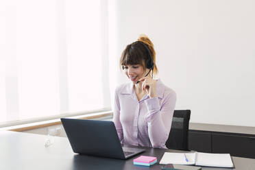 Geschäftsfrau mit Headset und Laptop am Schreibtisch - PNAF05258